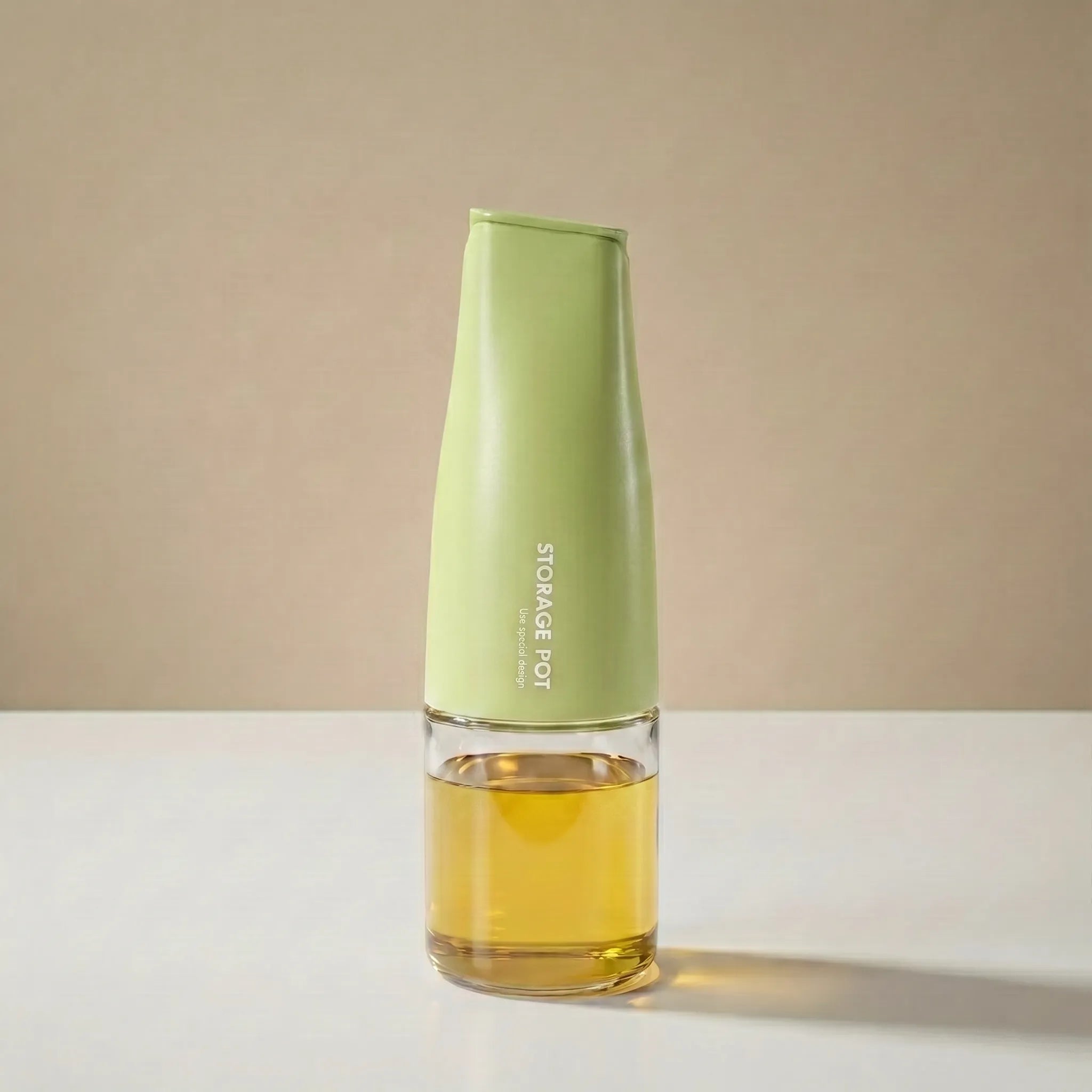 A modern green-capped cooking oil dispenser for kitchen made of glass and stainless steel filled with golden olive oil and shown against a neutral backdrop