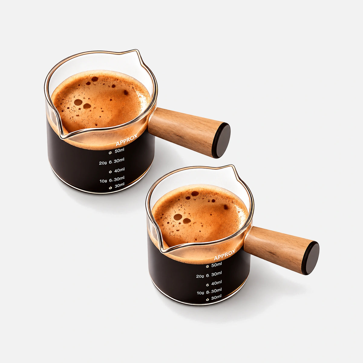 Two glass espresso measuring cups with wooden handles and dual pouring spouts.