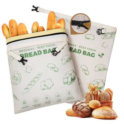 A set of two reusable beeswax bread bags is displayed, featuring a light-colored fabric with green illustrations of various bread types. The bags are partially filled with fresh baguettes, showcasing their practical design for food storage.#Green