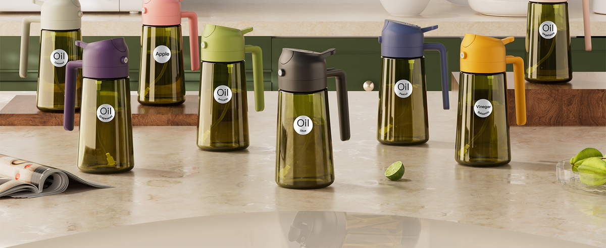 Dark green glass oil sprayers with purple, green, gray and yellow lids on a kitchen counter.