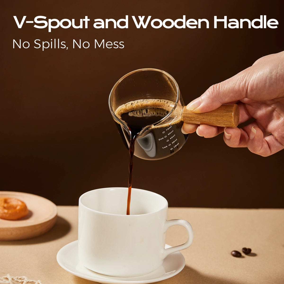 Espresso poured from the V-shaped spout of a wooden-handle glass measuring cup into a white mug.