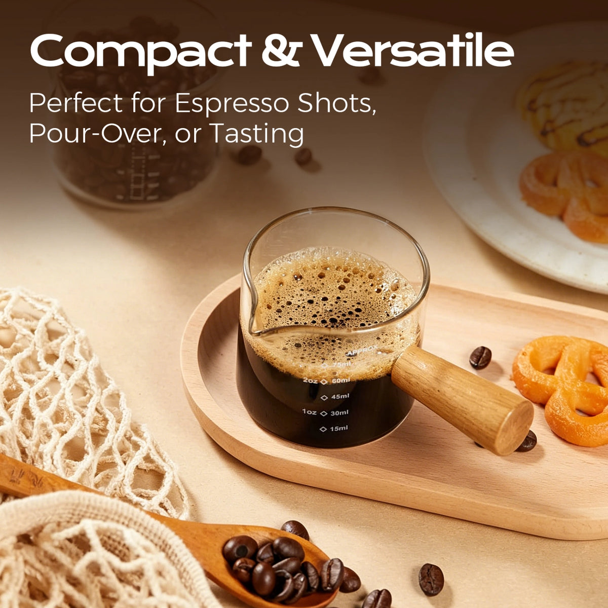 Small wooden-handle glass measuring cup filled with espresso on a wooden tray beside cookies.