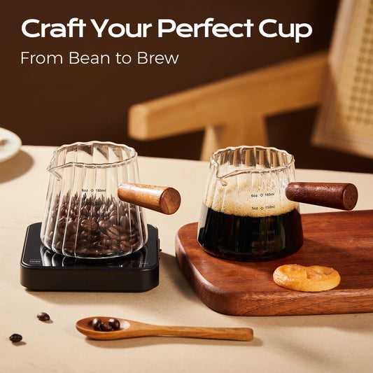 Fluted glass pitchers with wooden handles holding coffee beans and espresso, with one pitcher on a scale.