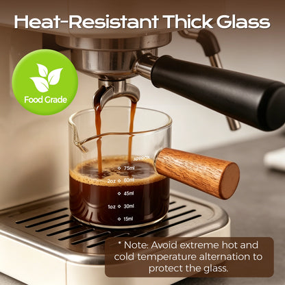 Espresso flowing from a coffee machine into a glass measuring cup with a wooden handle.