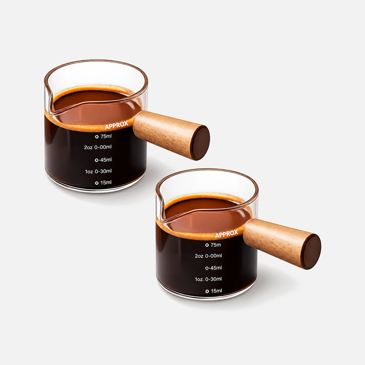 Two glass espresso measuring cups with wooden handles and single pouring spouts.
