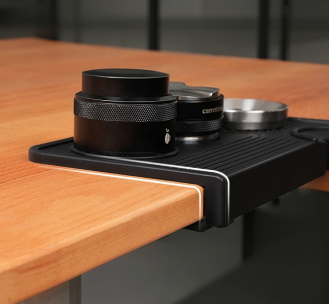 Counter edge lip on the black tamping mat; coffee tools shown for demonstration.