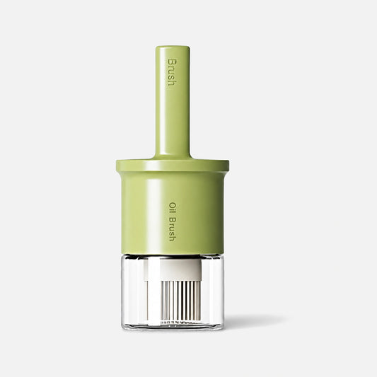 Glass oil dispenser with a green silicone brush and handle.