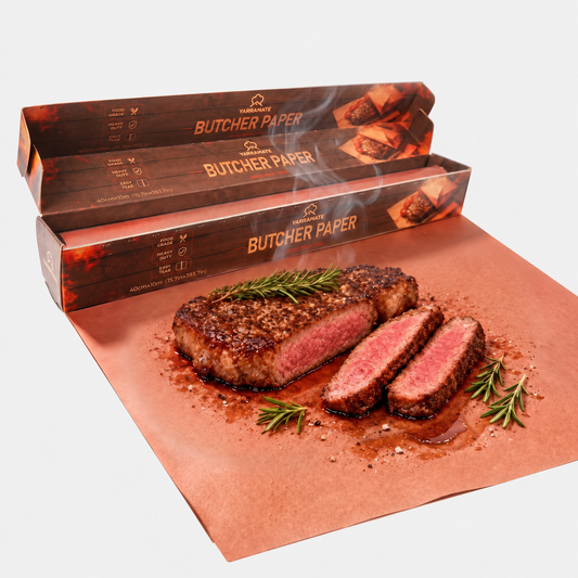 One pink butcher paper roll in a serrated dispenser box with a sheet displayed on a light gray background; steak and herbs are styling props, not included